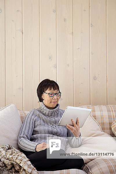 Ältere Frau benutzt Tablet-Computer  während sie zu Hause auf dem Sofa sitzt
