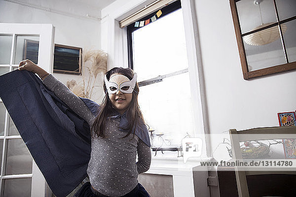 Portrait of girl wearing eye mask and cape while standing at home