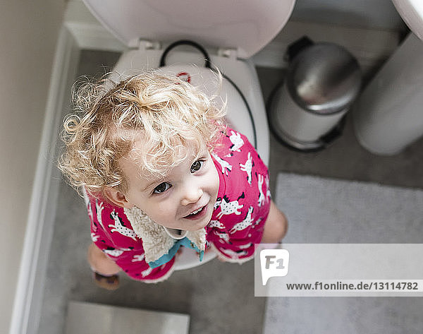 Portrait of happy girl sitting on toilet in bathroom