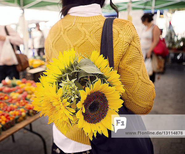 Rückansicht einer Frau mit Sonnenblumen im Portemonnaie auf dem Markt