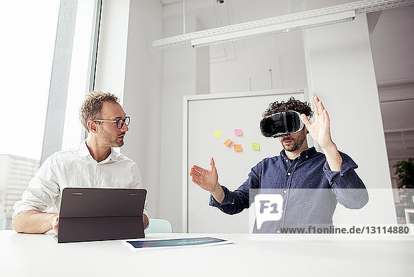 Ingenieur mit Tablet-Computer sieht Mitarbeiter an  der einen Virtual-Reality-Simulator im Büro untersucht