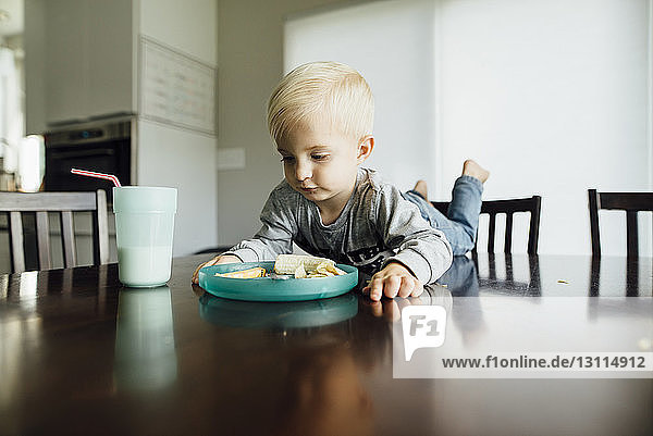 Kleiner Junge isst zu Hause auf dem Tisch liegend