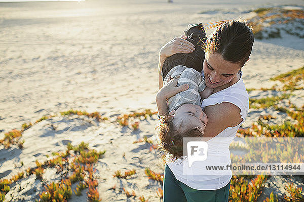 Hochwinkelansicht einer spielerischen Mutter  die ihren Sohn am Strand trägt