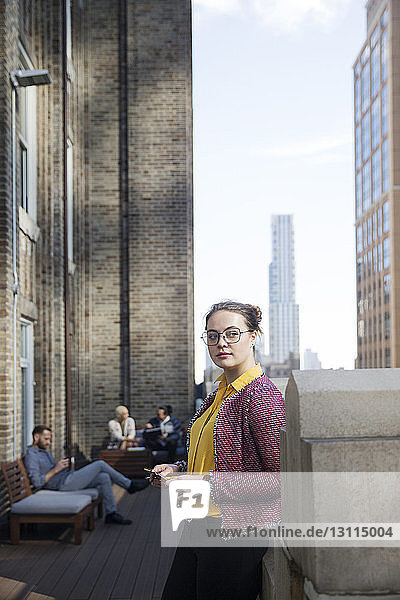 Woman with mobile phone looking away while colleagues sitting in background