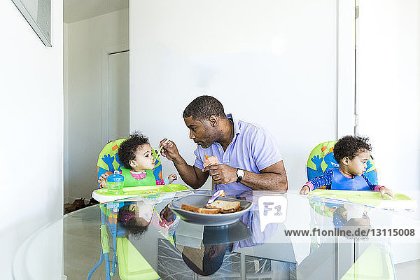Vater füttert Mädchen  während die Tochter am Tisch sitzt