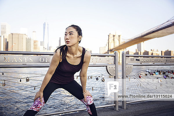 Nachdenkliche Sportlerin trainiert auf der Promenade mit der Brooklyn Bridge und dem One World Trade Center im Hintergrund