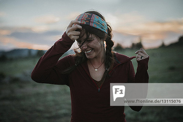 Glückliche Frau entfernt Stirnband  während sie bei Sonnenuntergang auf dem Feld steht