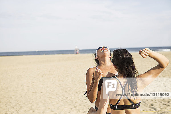 Female friends enjoying at beach against sky