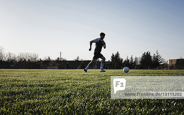 Man practicing soccer on grassy field against clear sky at park during sunset