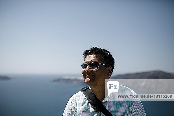Lächelnder Mann mit Sonnenbrille  während er am sonnigen Tag gegen Meer und Himmel schaut