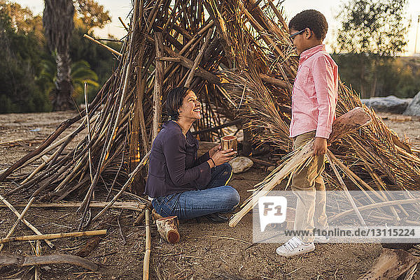 Mutter und Sohn bauen Hütte im Wald bei Sonnenuntergang