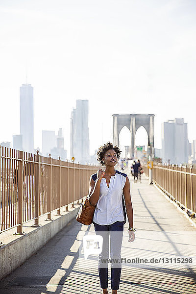 Nachdenkliche Frau geht auf einem Fußweg mit der Brooklyn Bridge und dem One World Trade Center im Hintergrund