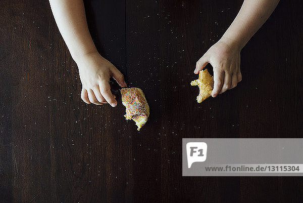 Cropped hands of boy holding bread on table at home
