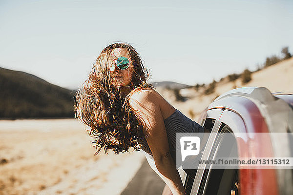 Seitenansicht einer jungen Frau mit zerzaustem Haar  die sich aus dem Autofenster lehnt