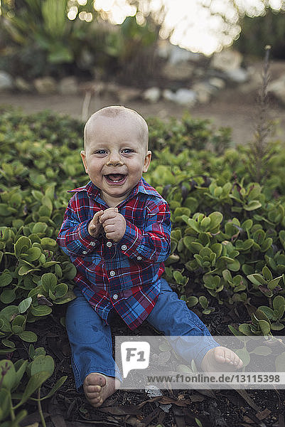 Porträt eines fröhlichen kleinen Jungen  der inmitten von Pflanzen im Park sitzt