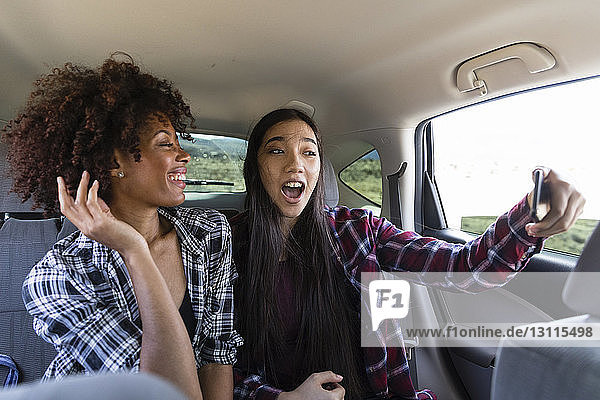 Happy female friends talking selfie while traveling in car