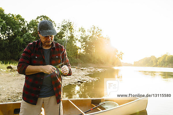 Mittelgroßer erwachsener Mann  der am Seeufer am Boot steht und seine Ausrüstung an der Angelschnur befestigt