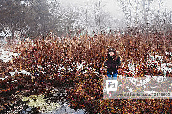Girl walking on grassy field by lake in forest during winter