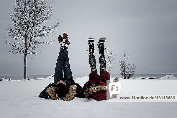 Friends lying at snow covered beach against sky during winter