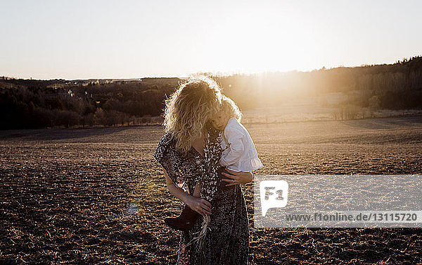 Mutter trägt Tochter  während sie bei Sonnenuntergang auf dem Feld steht