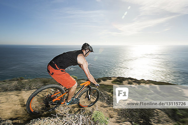 Side view of athlete riding bicycle on rock by sea