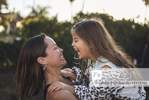 Happy mother and daughter looking at each other in yard during sunset