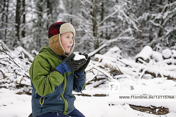 Boy eating snow while kneeling on field