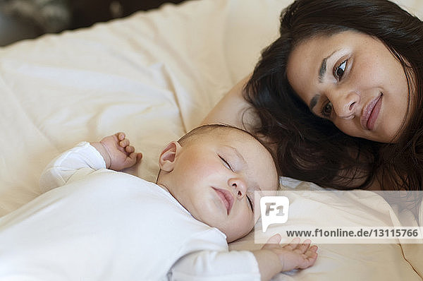 Mother looking at daughter sleeping on bed at home