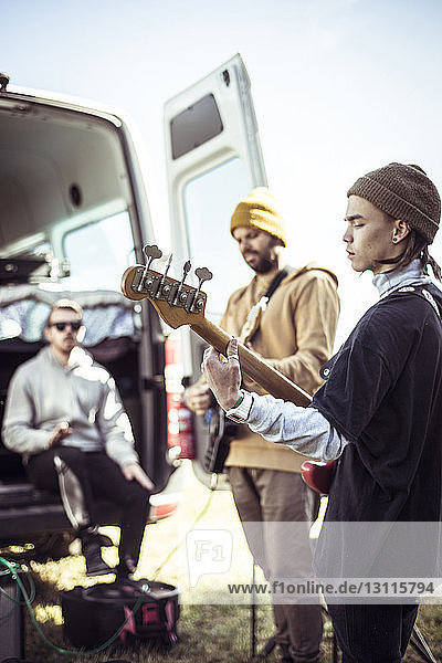 Friends playing guitar while man sitting in trailer home on field against sky