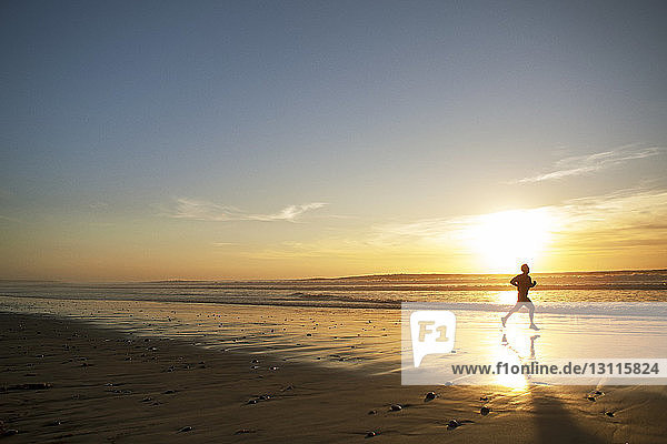 Side view of male athlete running on beach during sunset