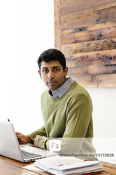 Porträt eines Geschäftsmannes mit Laptop und Buch am hölzernen Konferenztisch
