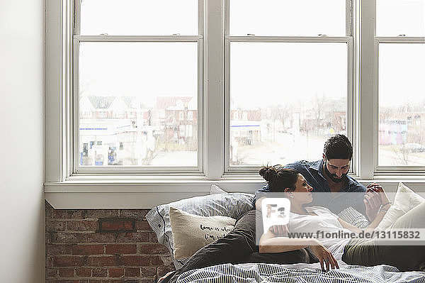 Romantic couple relaxing on bed by window at home