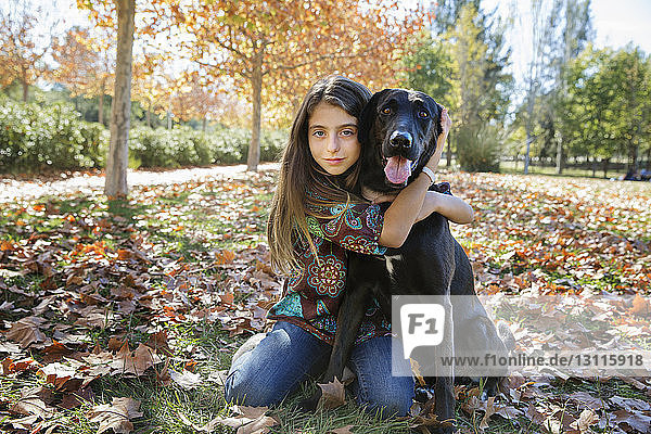 Porträt eines Mädchens mit schwarzem Hund  das im Herbst im Park sitzt