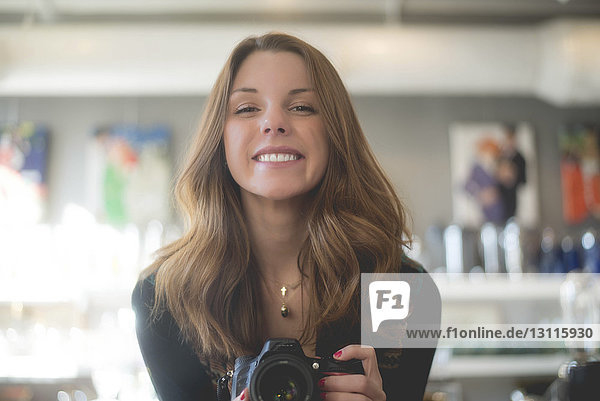 Portrait of happy woman holding camera while standing at home