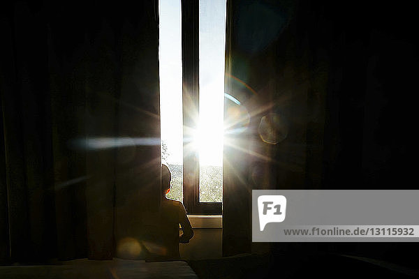 Ausgeschnittenes Bild eines Jungen  der zu Hause am Fenster steht und durch die Tür gesehen wird