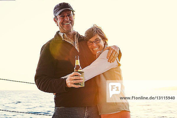 Portrait of smiling couple embracing while standing on boat against clear sky