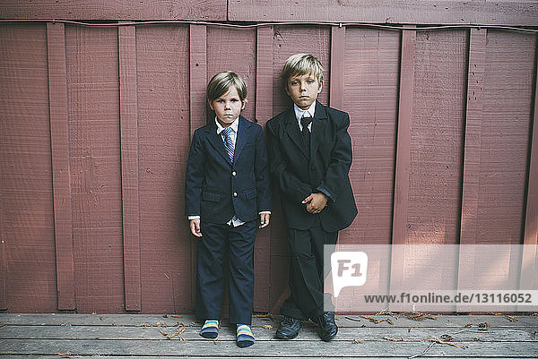 Porträt selbstbewusster Brüder in Anzügen  die an einer Holzwand stehen