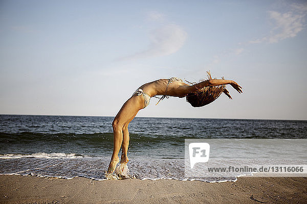Frau macht Rückwärtssalto am Strand gegen den Himmel