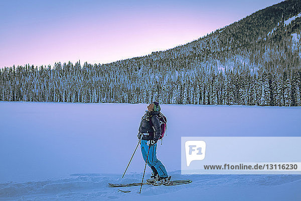 Tired female skier standing on snow covered field against trees