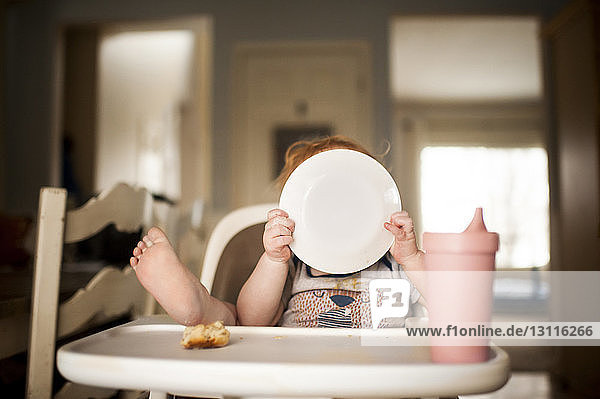 Baby boy holding plate while sitting on high chair at home