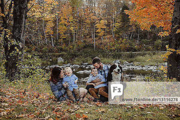 Parents enjoying with sons by dog on grassy field in forest during autumn