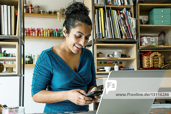 Glückliche Geschäftsfrau benutzt Smartphone  während sie im Büro steht