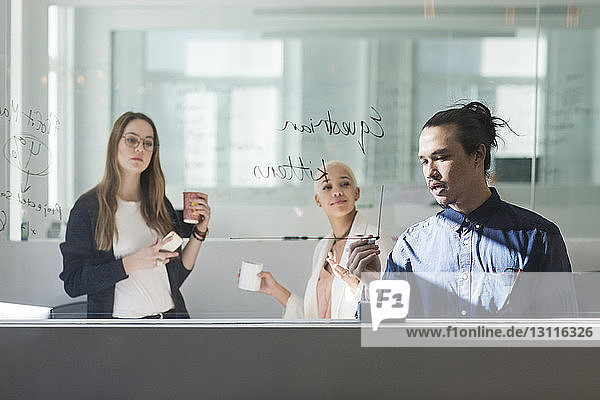Businesswomen looking at colleague writing on window in office