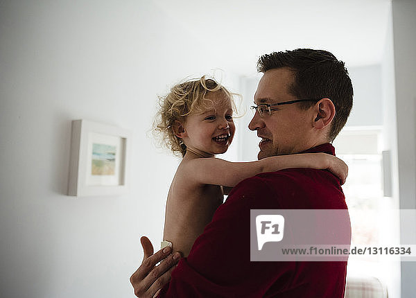 Father carrying happy daughter while standing by wall at home