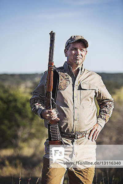 Portrait of hunter holding rifle while standing against sky