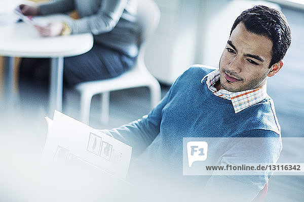 Confident businessman reading document while sitting in office