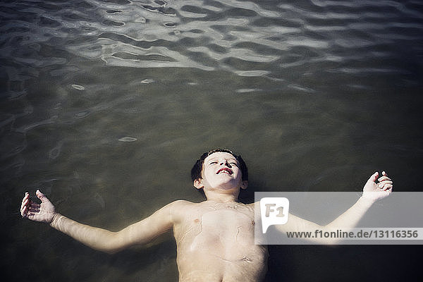 Draufsicht auf einen Jungen ohne Hemd  der bei Sonnenschein auf dem Meer treibt