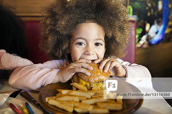 Porträt eines Mädchens  das im Restaurant Burger auf dem Tisch isst