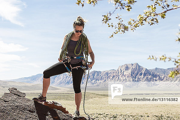 Full length of woman tightening safety harness while standing against mountains at Red Rock Canyon National Conservation Area