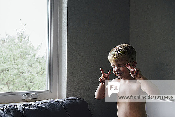 Junge gestikuliert  während er zu Hause am Fenster sitzt